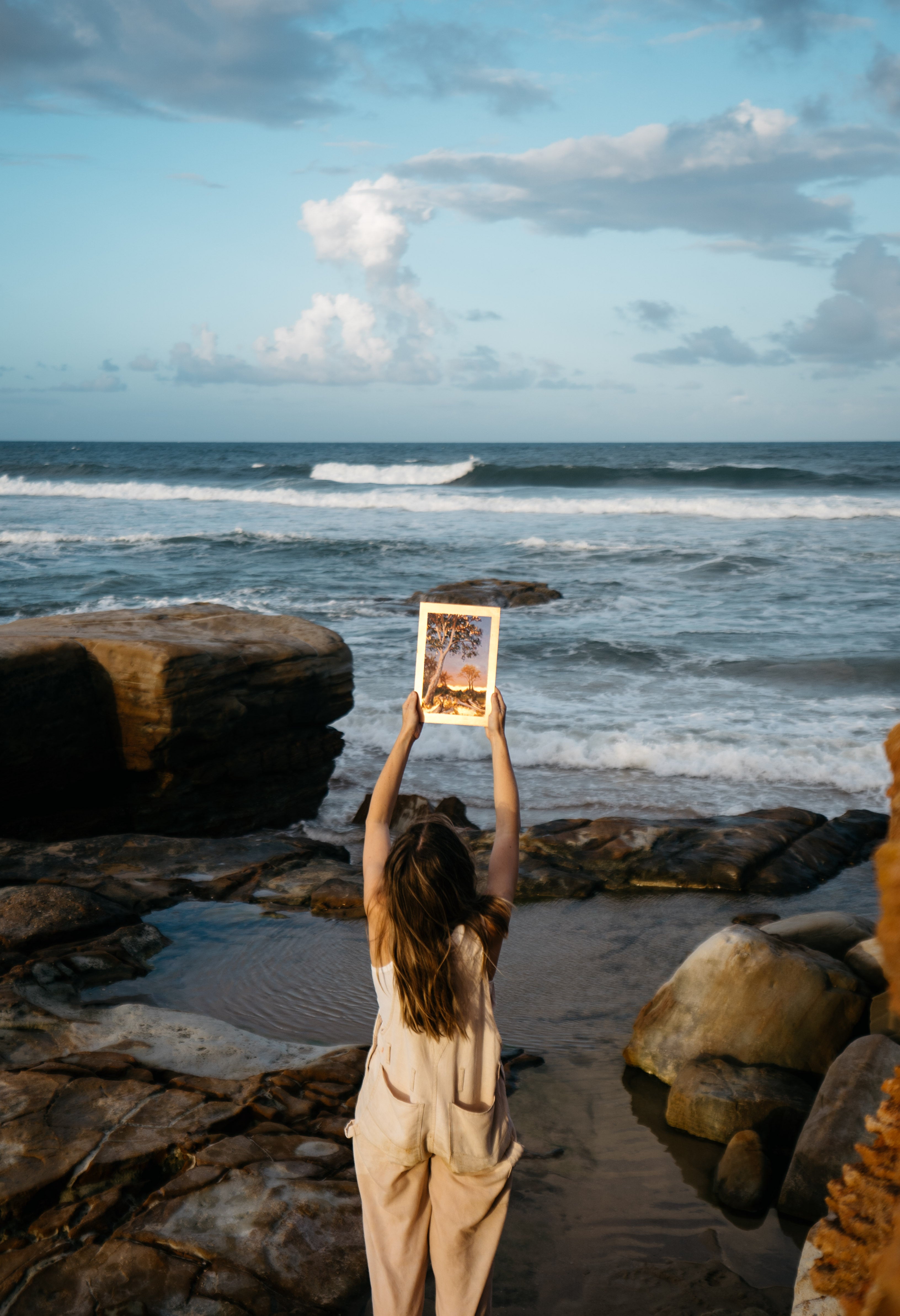 Person holding a painting up to the light at sunset at the beach